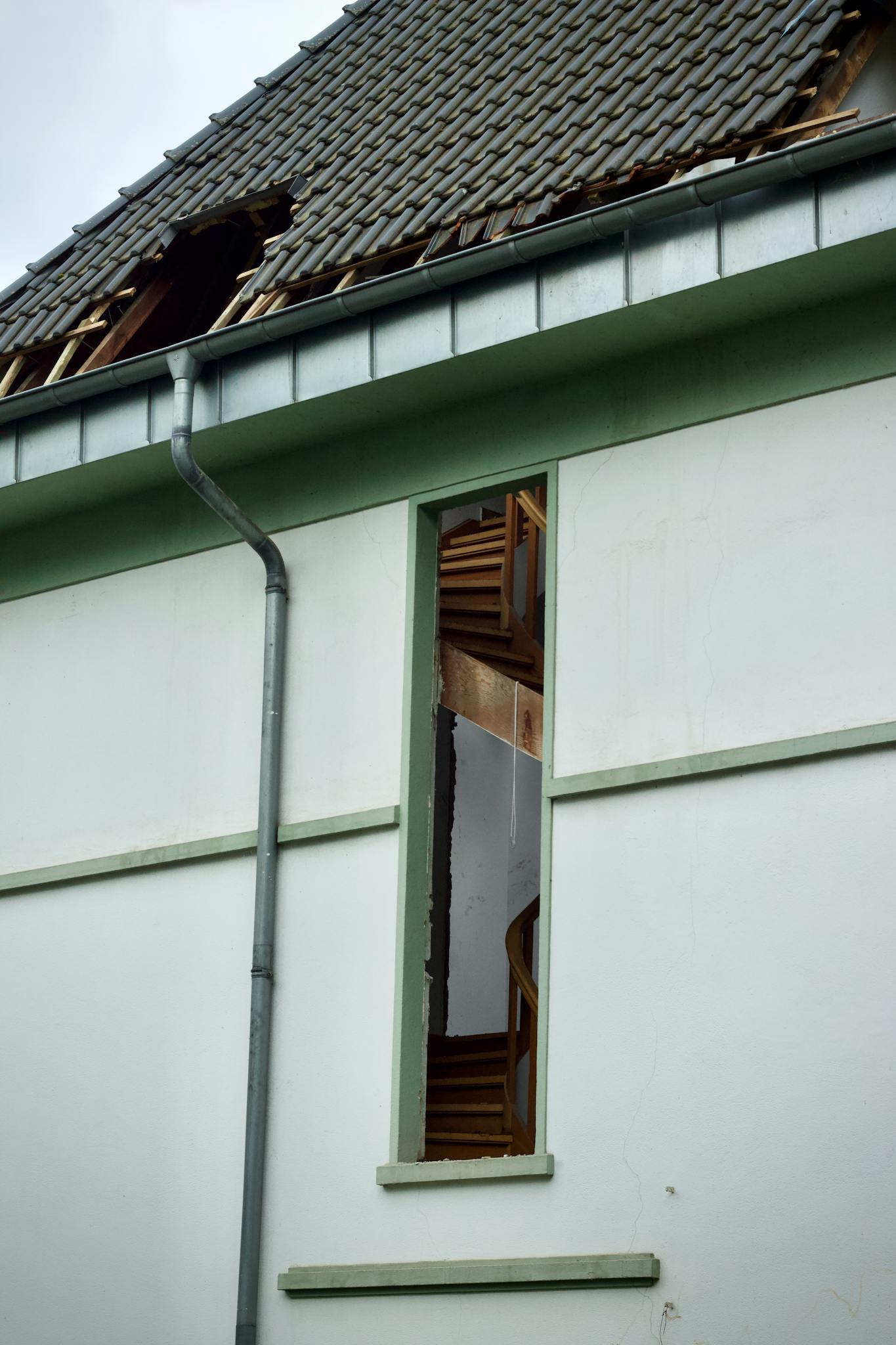 An exterior view of a damaged house showing a broken roof and exposed interior structure.
